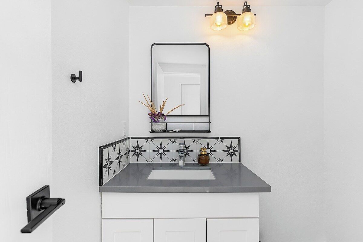 A bathroom with a white sink, black and white patterned backsplash, and a mirror above it.