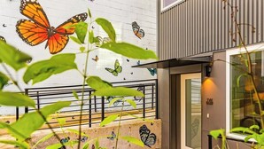 Un bâtiment dont la façade extérieure est ornée d’une fresque représentant des papillons, avec une porte d’entrée en verre et un garde-corps en métal.