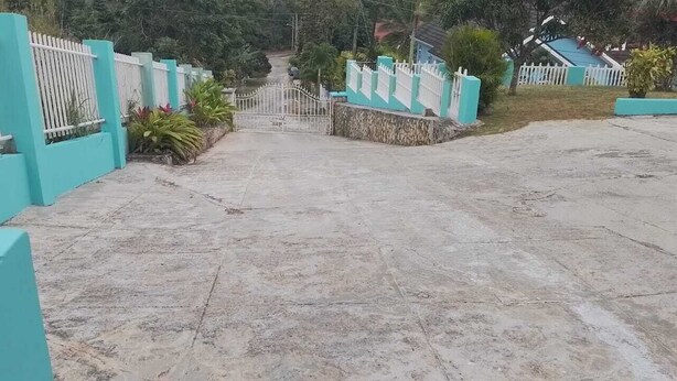 A paved driveway leading to a gated entrance with a white fence and a gate. - Beautiful One Bedroom with WiFi in Brumalia Mandeville, Manchester (Mandeville)