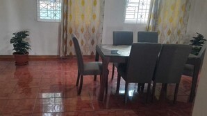 A dining area with a table and chairs, a potted plant, and a window with curtains. - Beautiful One Bedroom with WiFi in Brumalia Mandeville, Manchester (Mandeville)