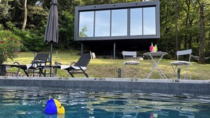 Un espace piscine extérieur moderne, doté de chaises longues, d’une petite table et d’un bâtiment avec de grandes fenêtres.