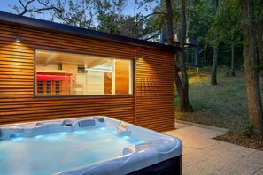 Une cabane moderne en bois, dotée d’un jacuzzi et d’une porte en verre donnant sur un intérieur rouge.