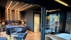 Una habitación de hotel moderna con una cama grande, una zona de estar con sofás, una mesita y una bañera.