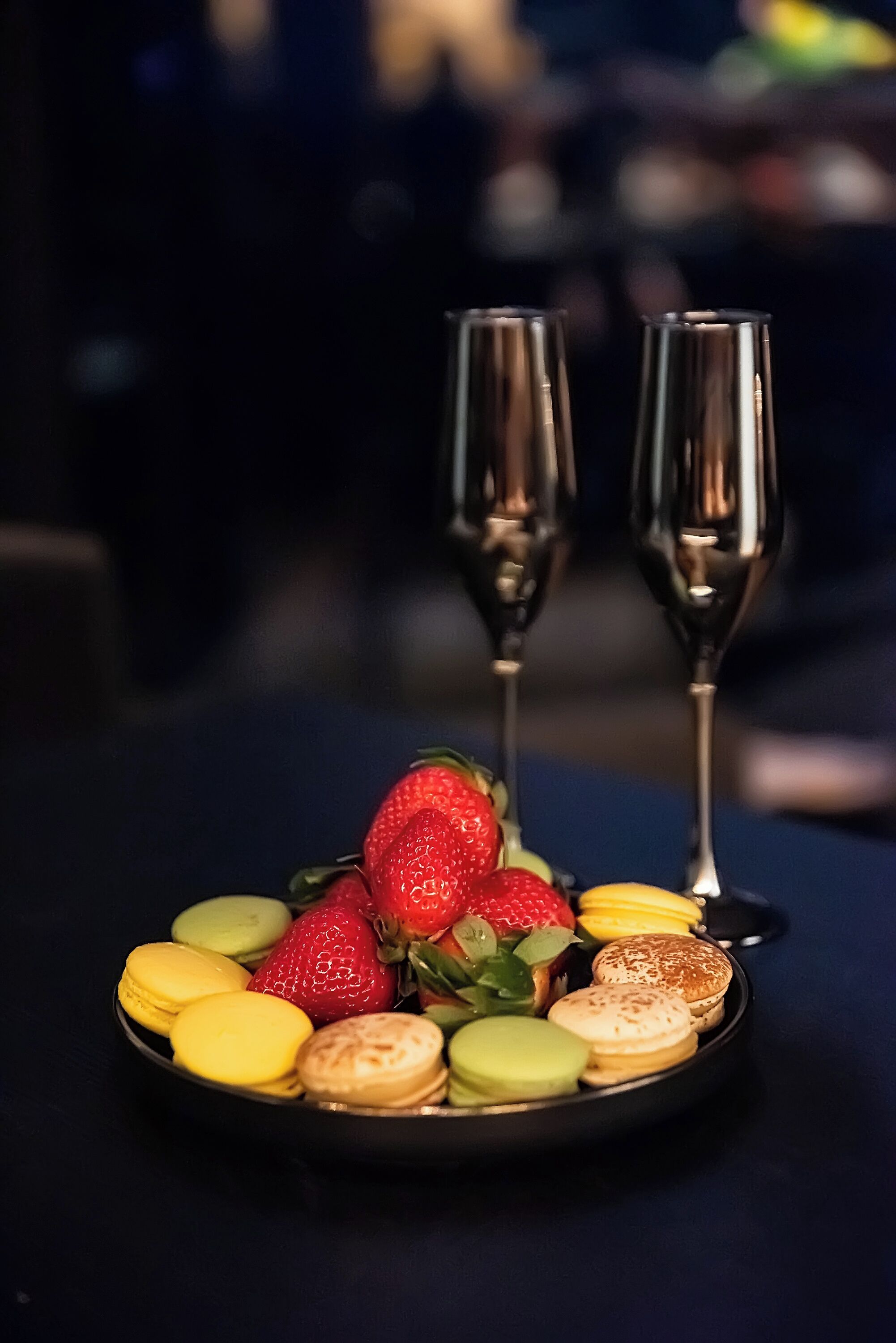 Une assiette de desserts comprenant des fraises, des macarons et une bouteille de champagne, le tout posé sur une table.