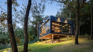 Una estructura moderna de madera elevada, con amplios ventanales de vidrio, rodeada de árboles y césped.