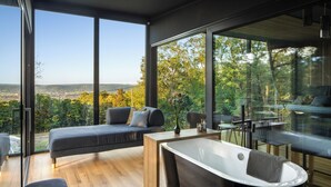 Un dormitorio moderno con un ventanal grande, un sofá, una bañera y un comedor.