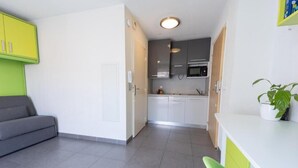 A compact living space with a kitchenette, grey sofa, and a green chair. - Le Campus Appartement (Nice)