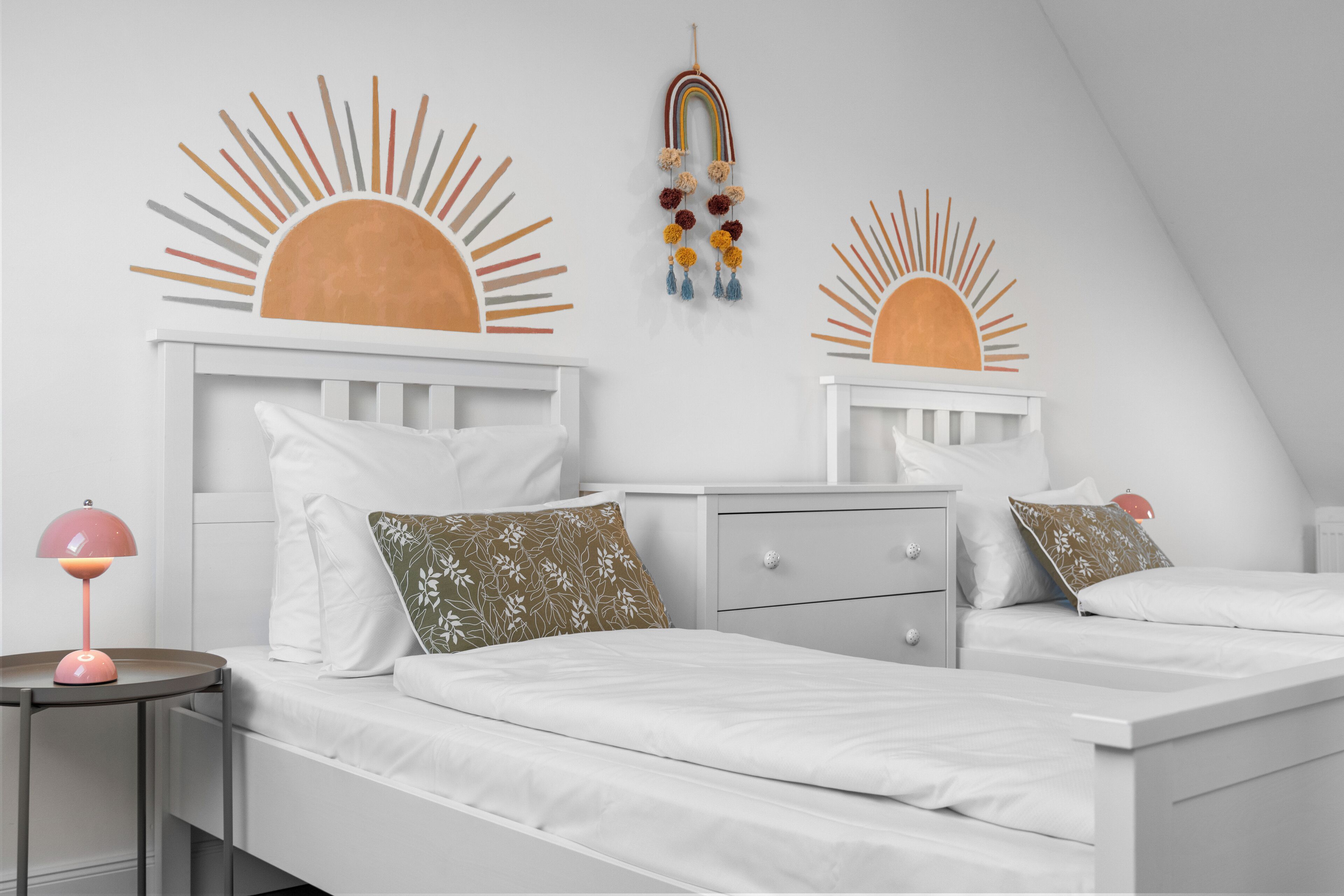 Ein Schlafzimmer mit zwei Betten, weißer Bettwäsche, einem Nachttisch mit Lampe und Wandbildern.