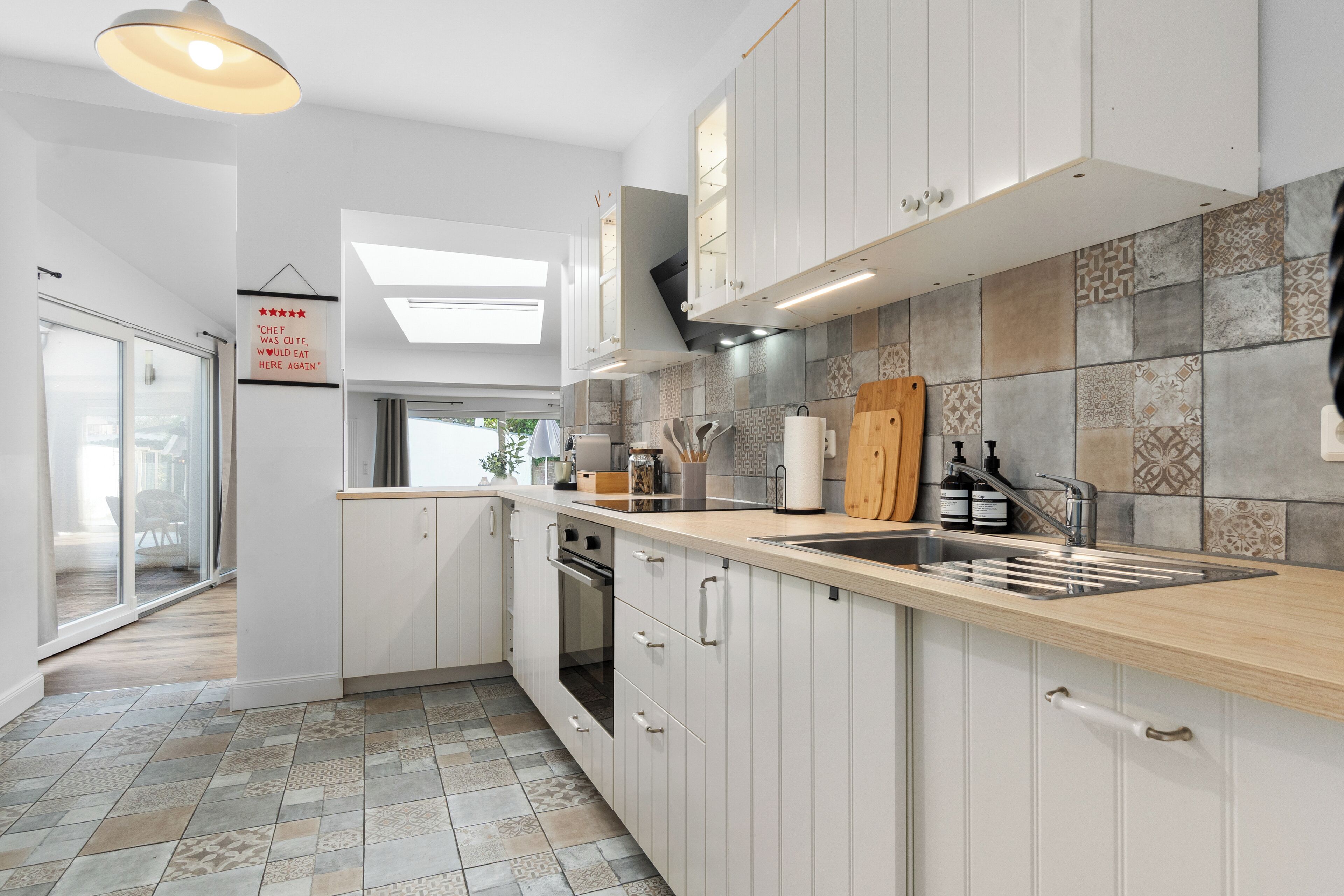 A modern kitchen with white cabinets, a wooden countertop, and a tiled backsplash.