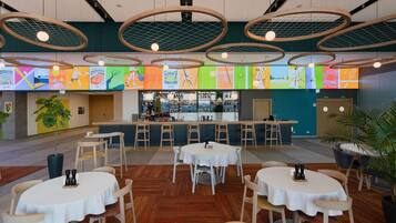 A modern restaurant with round tables, a bar area, and a colorful mural on the wall.
