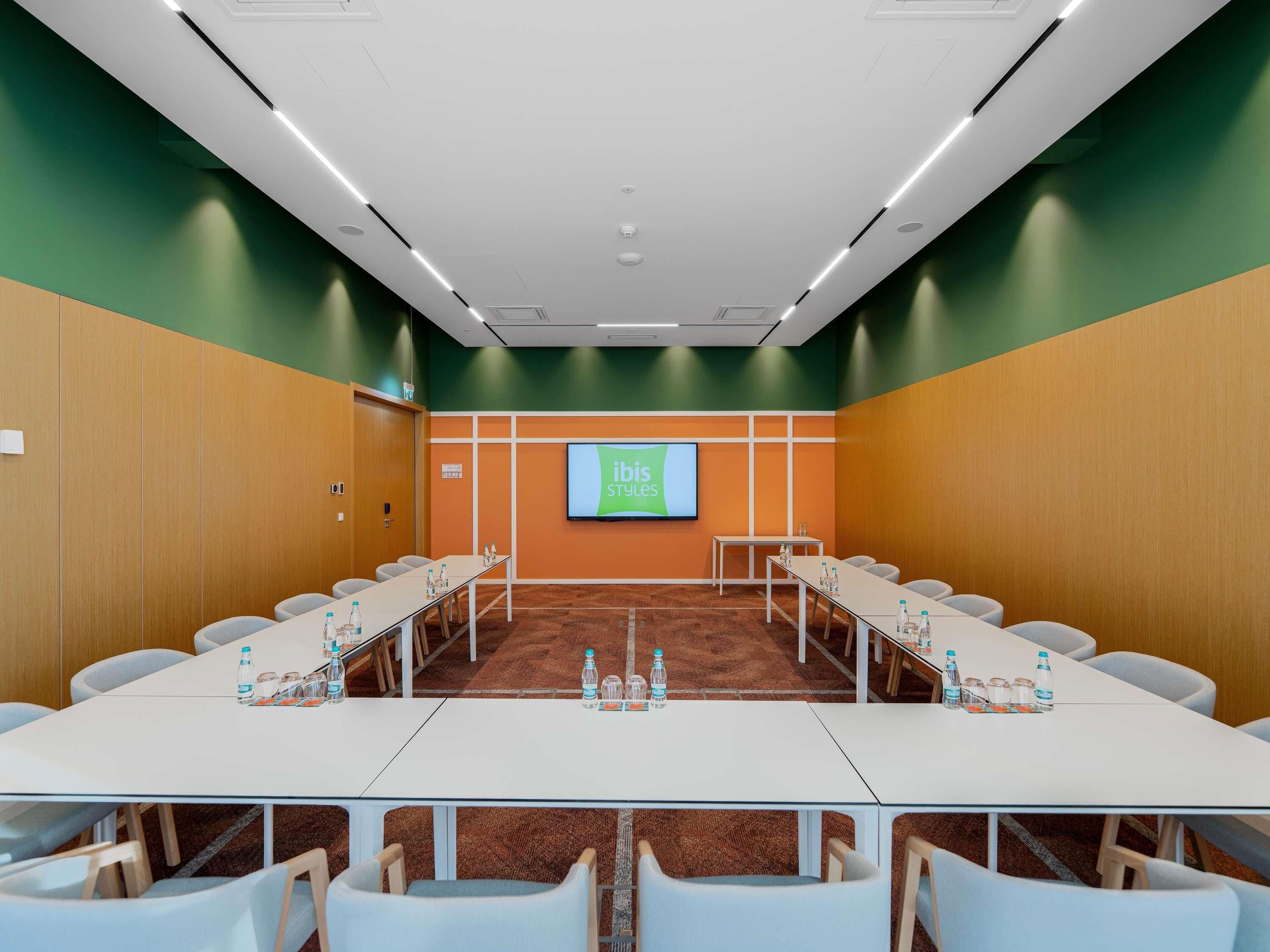 A conference room with a long table, chairs, a projector screen, and a carpeted floor.