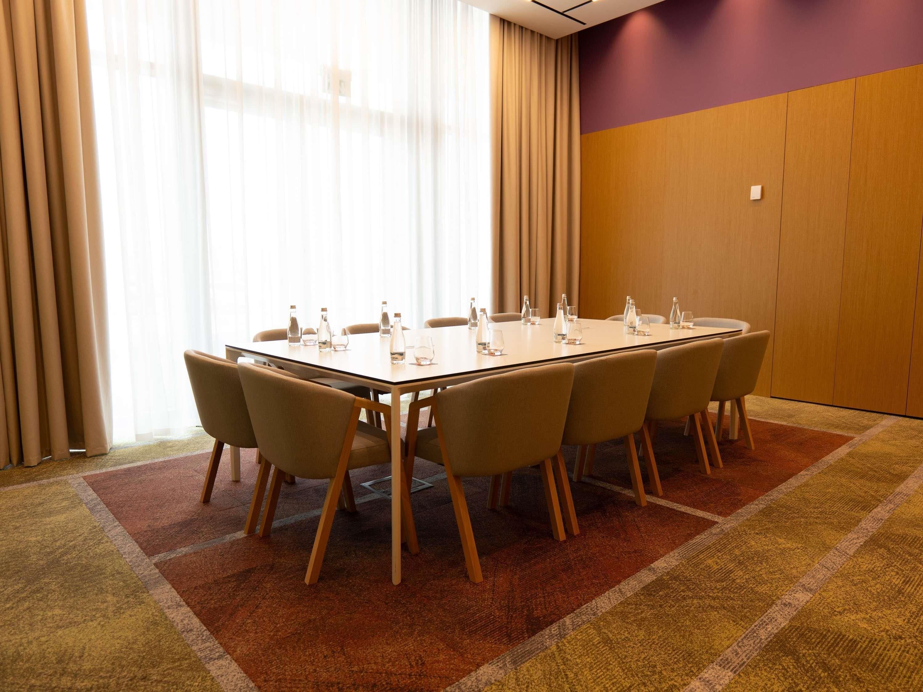 Sala de conferências com uma mesa comprida, cadeiras e garrafas de água.