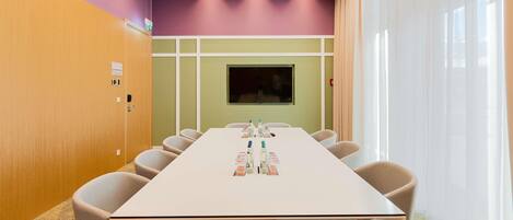 A conference room with a long table, chairs, a television screen, and a window with curtains.