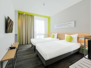 A hotel room with two beds, a desk, a chair, a TV, and a window with curtains.