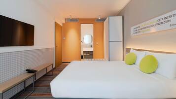 A modern hotel room with a bed, a bench, a mirror, a sink, and a television.