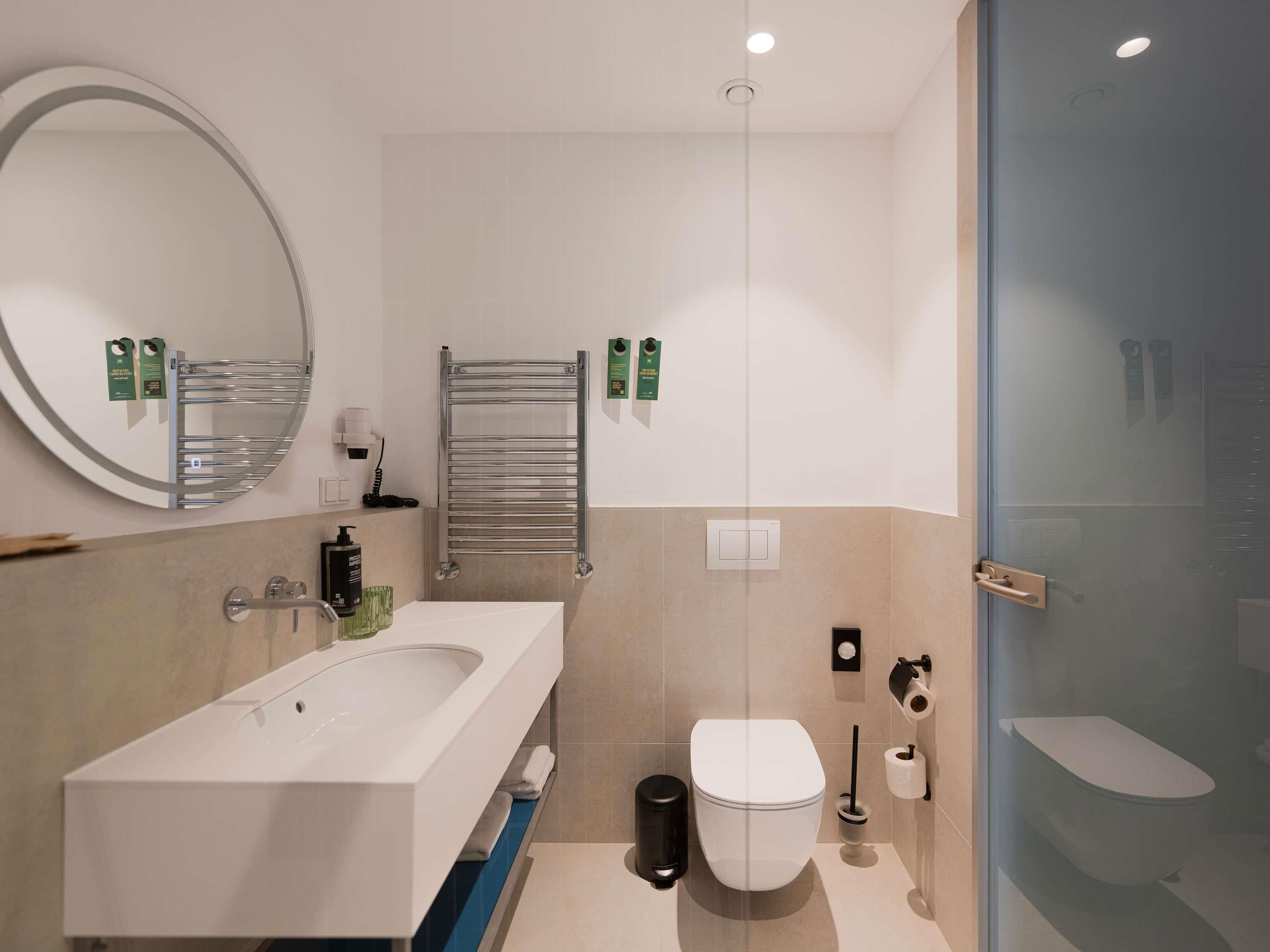 A modern bathroom with a sink, mirror, towel rack, toilet, and glass shower enclosure.