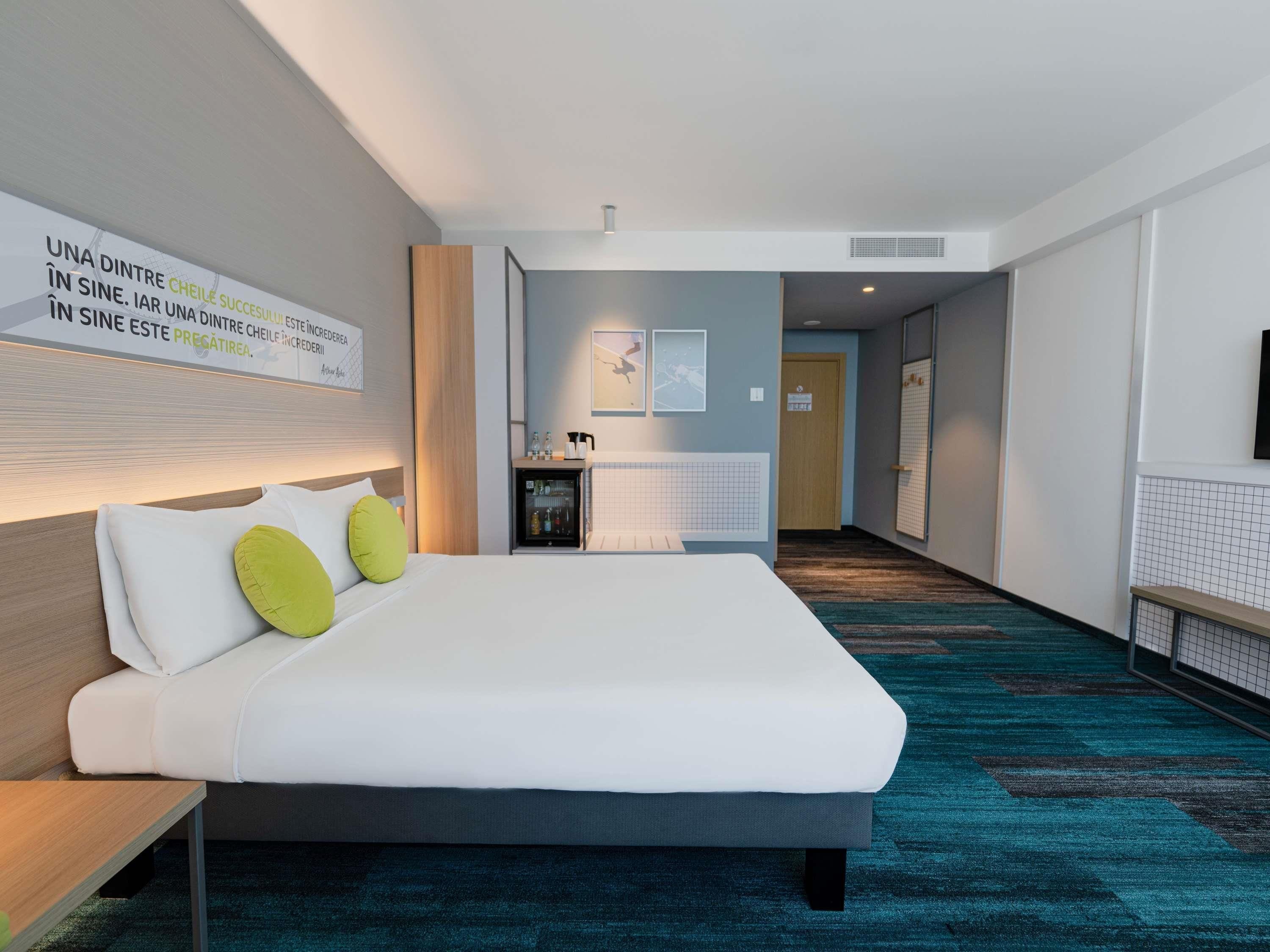 Ett hotellrum med en säng, ett skrivbord, en minibar och ett badrum som syns genom en öppen dörr.