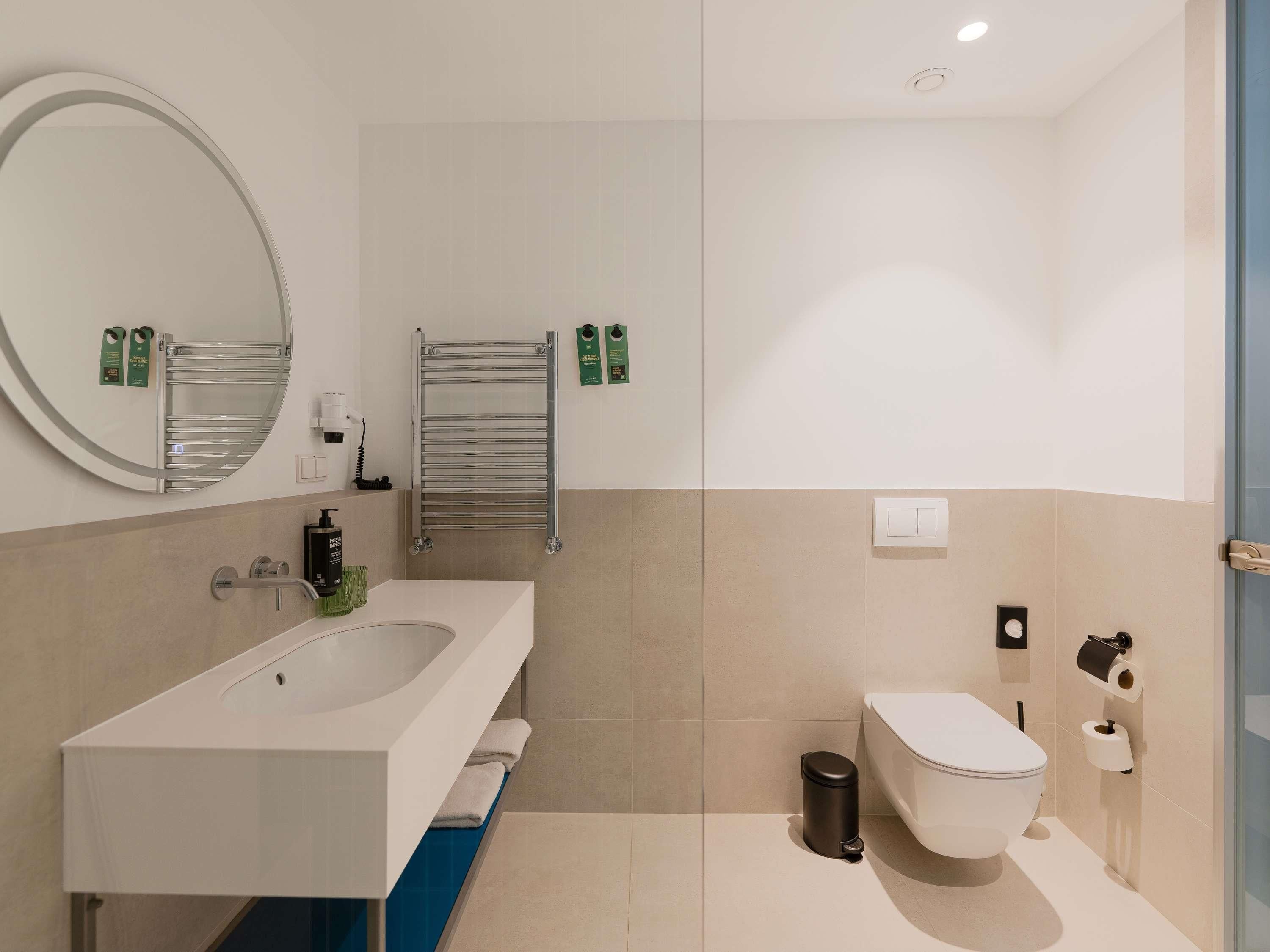 Un baño moderno con un lavamanos grande, espejo, toallero, inodoro y cubo de basura.