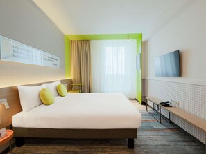 Une chambre d’hôtel avec un lit, une télévision, un bureau et une fenêtre avec des rideaux.