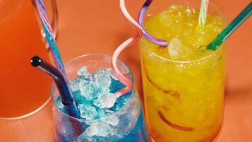 Two glasses of iced drinks with colorful straws on a table.