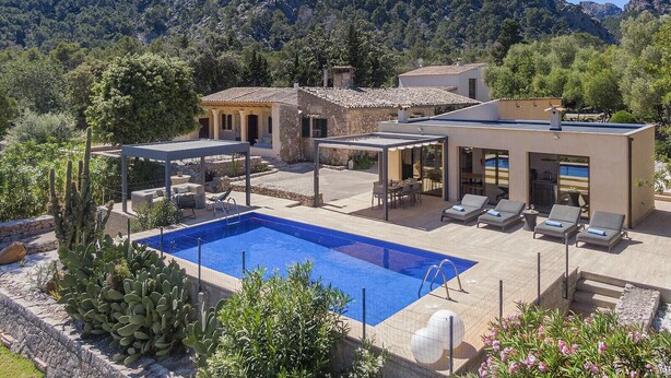 Un espace piscine avec des chaises longues, un bâtiment en pierre et une chaîne de montagnes en arrière-plan.