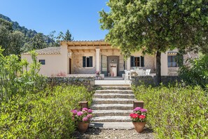 Une villa avec des marches en pierre menant à une entrée couverte, entourée d’une végétation luxuriante et de plantes en pot.