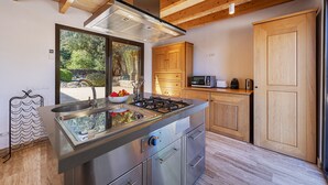 Une cuisine moderne dotée d’un îlot central, d’appareils électroménagers en acier inoxydable, de meubles de rangement en bois et offrant une vue sur la verdure environnante.