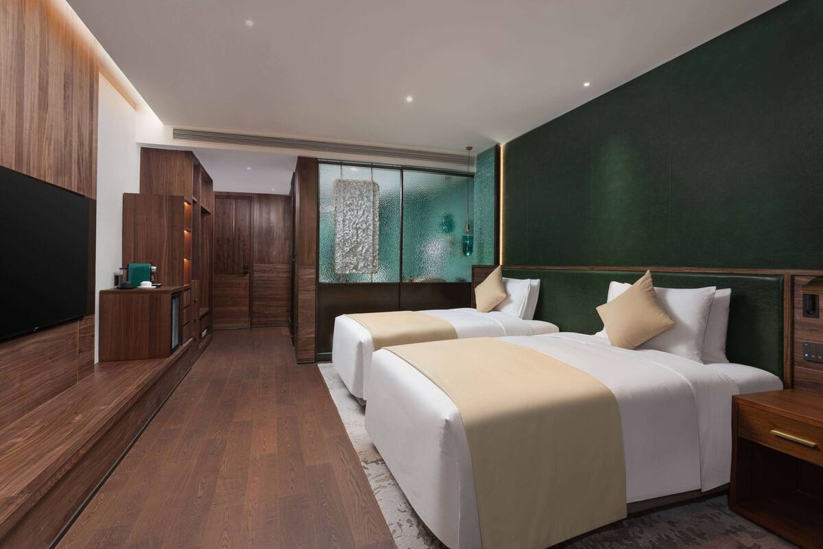 Habitación de hotel moderna con dos camas, un televisor, un armario de madera y un ventanal con vistas.