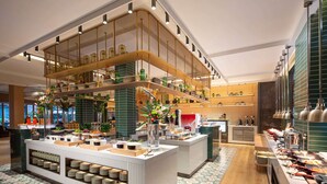 Een moderne hotel lobby met een centraal eiland, diverse zithoeken en verschillende voorzieningen, waaronder een buffet en een koffiehoek.