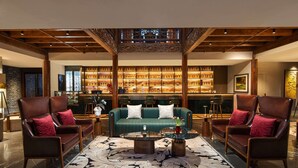 Een hal met een groene bank, twee fauteuils, een bijzettafeltje en een bar met flessen op de planken.