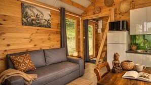 Ein gemütliches Blockhauss-Interieur mit Sofa, Esstisch, Küchenzeile und einem großen Fenster.