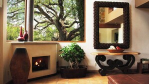 A room with a fireplace, a large window with a tree view, a mirror, and a plant. - Serene Oasis in San Miguel de Allende 6-bedroom Villa With Hot Tub (San Miguel de Allende)