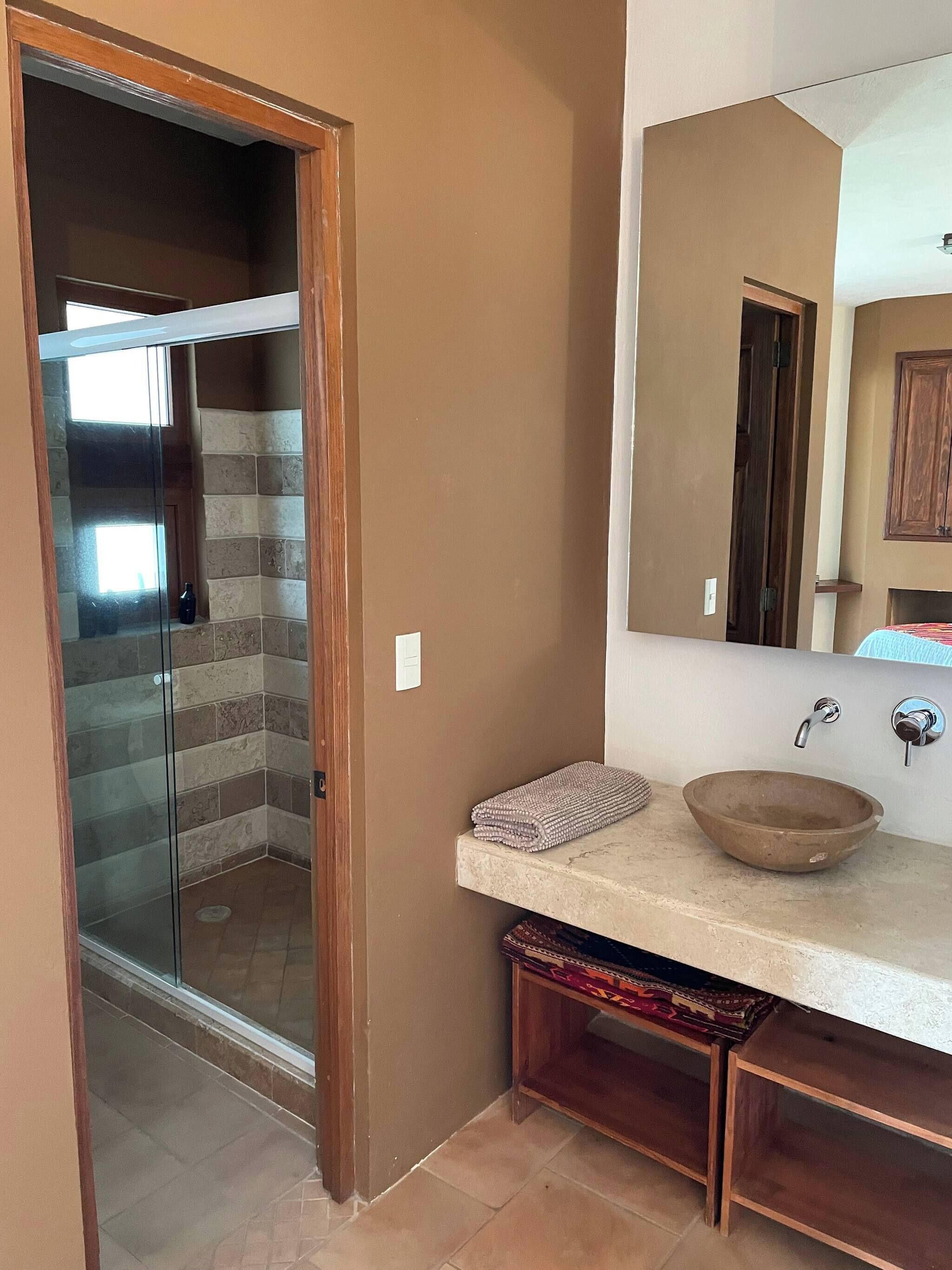 A bathroom with a glass shower door, a wooden vanity, a sink with a bowl, and a mirror.