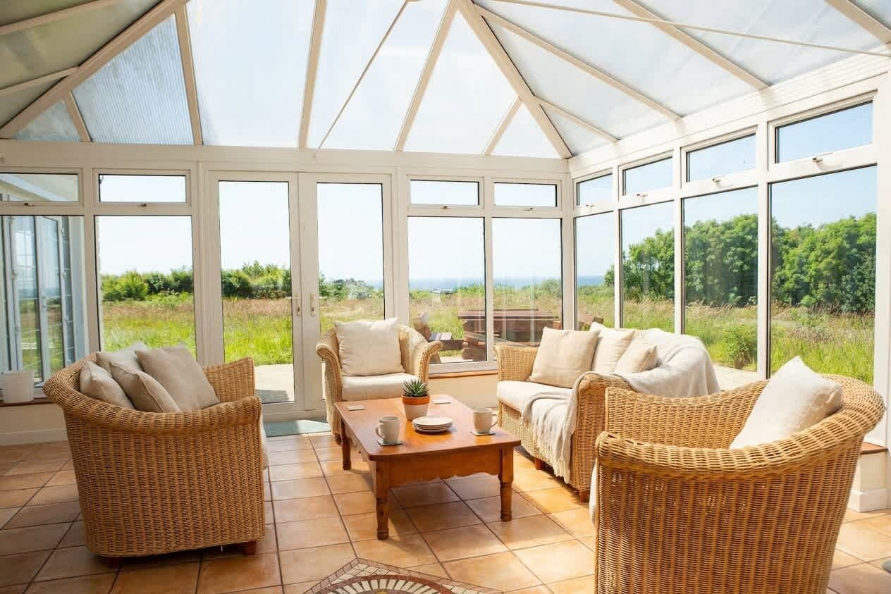 A conservatory with wicker furniture, a wooden coffee table, and a view of greenery.