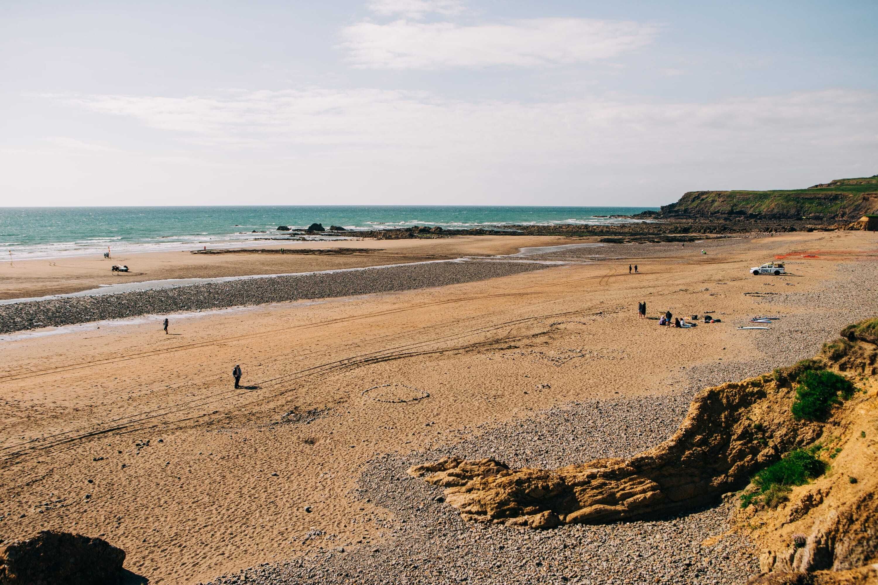 Une plage côtière avec un rivage rocheux, une zone de sable et quelques personnes qui se promènent.