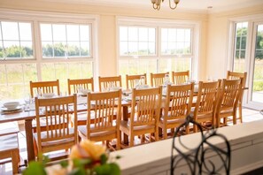 A dining area with wooden tables and chairs, large windows, and a view of greenery outside. - Spacious 6 Bed Holiday Cottage w Sea Views (Bude)