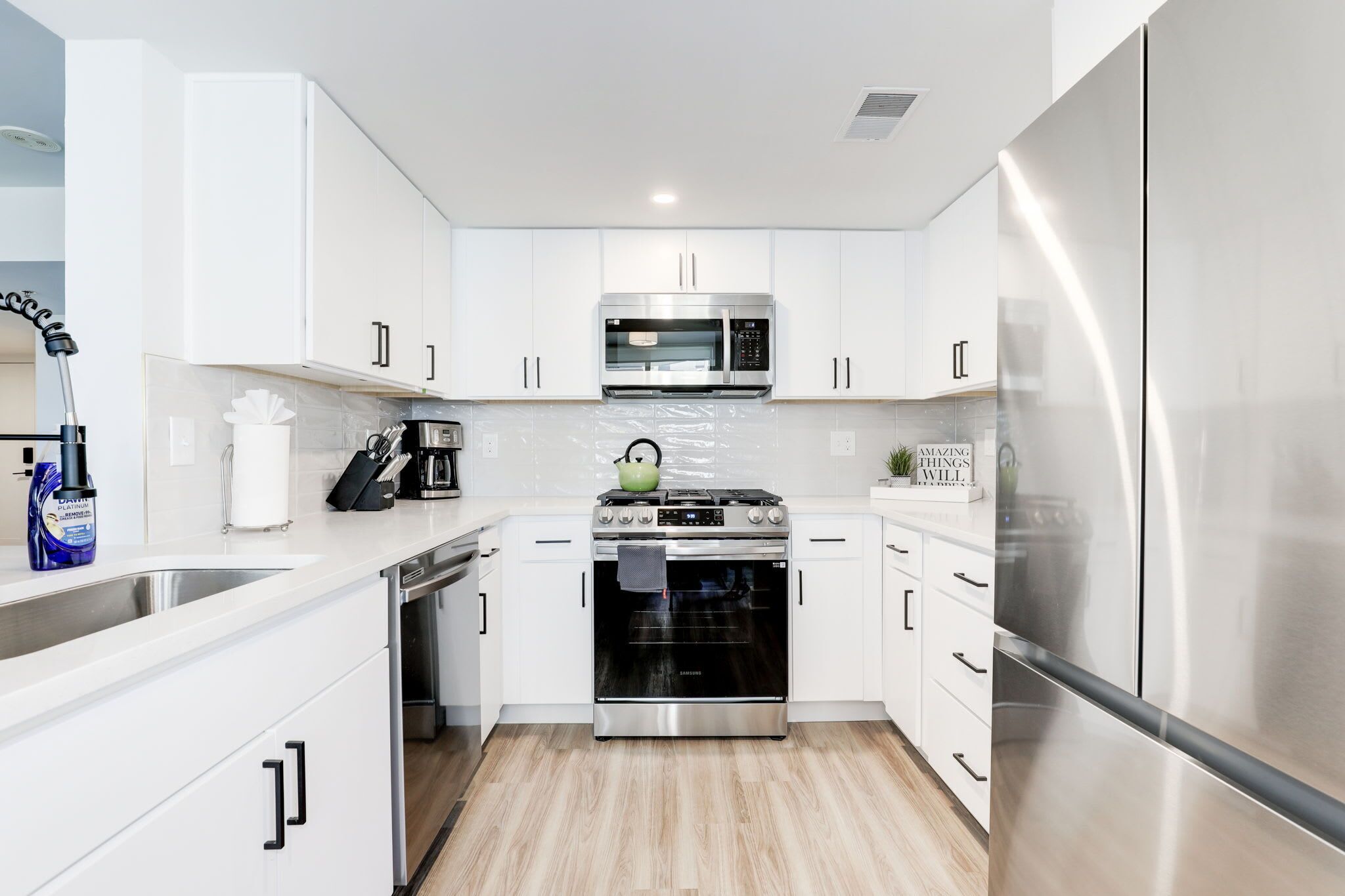 A modern kitchen with white cabinets, stainless steel appliances, and a wooden floor.