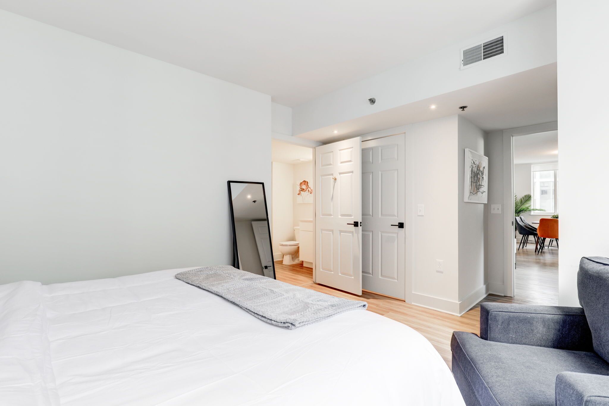 A modern bedroom with a large bed, a chair, and a door leading to a bathroom.