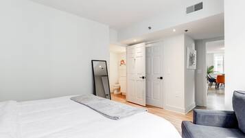 A modern bedroom with a large bed, a chair, and a door leading to a bathroom.