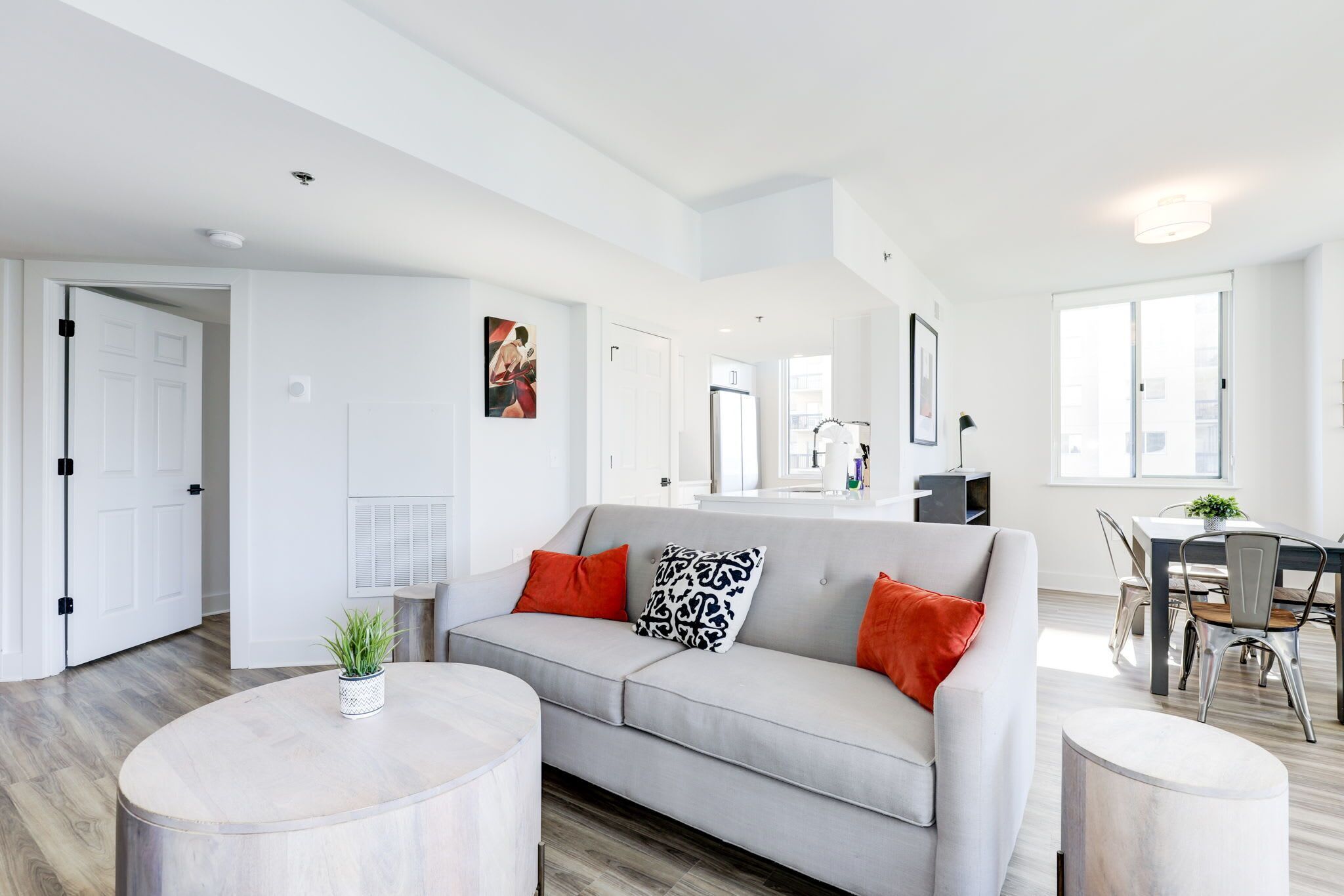 A modern living room with a grey sofa, round coffee table, and a dining area with a table and chairs.