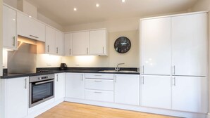 A modern kitchen with white cabinetry, a black countertop, and a stainless steel range hood.