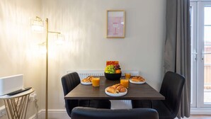 A dining area with a table set for breakfast, including croissants, juice, and a fruit bowl.