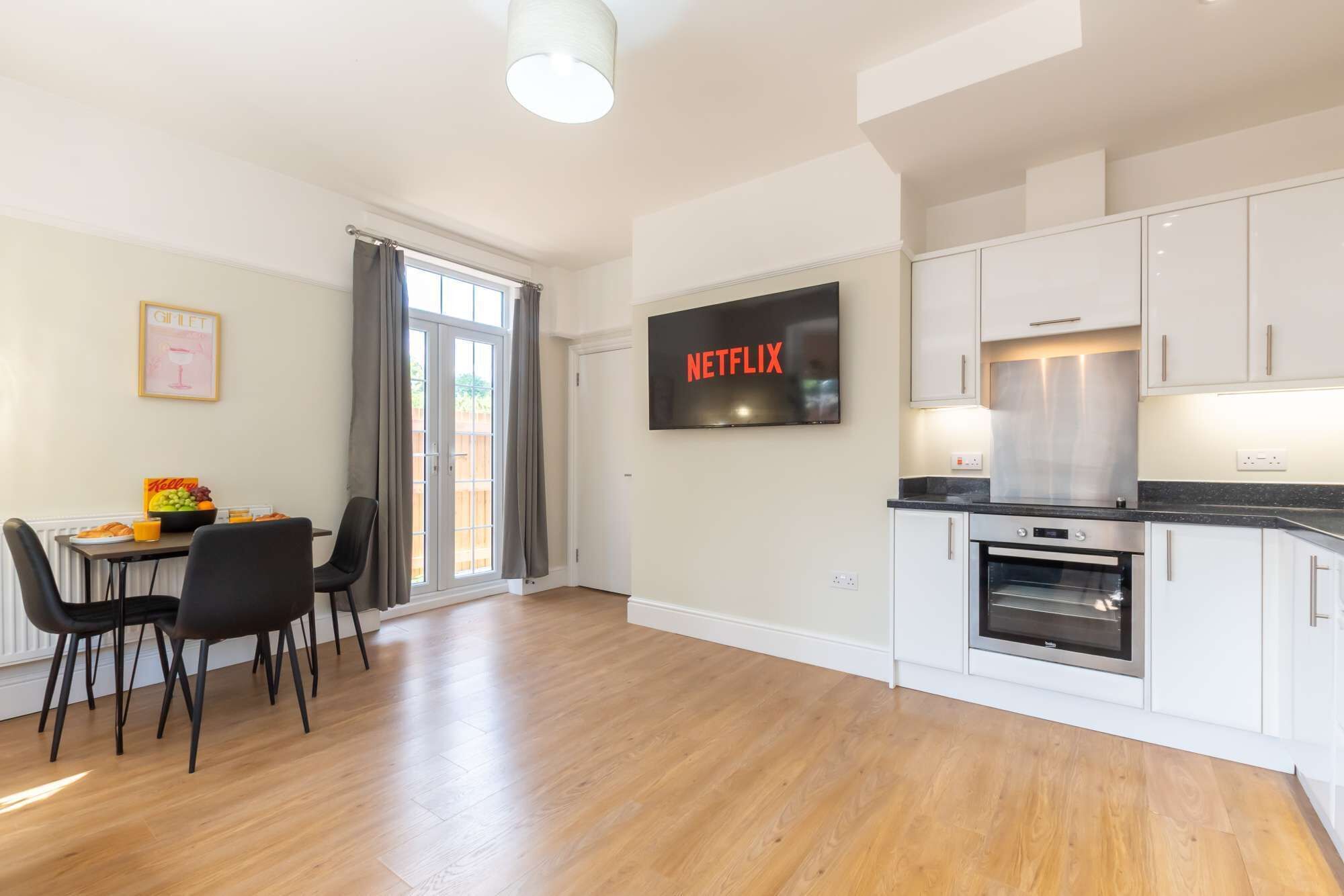 A modern kitchen with white cabinets, a built-in oven, and a flat-screen TV displaying 'NETFLIX'.