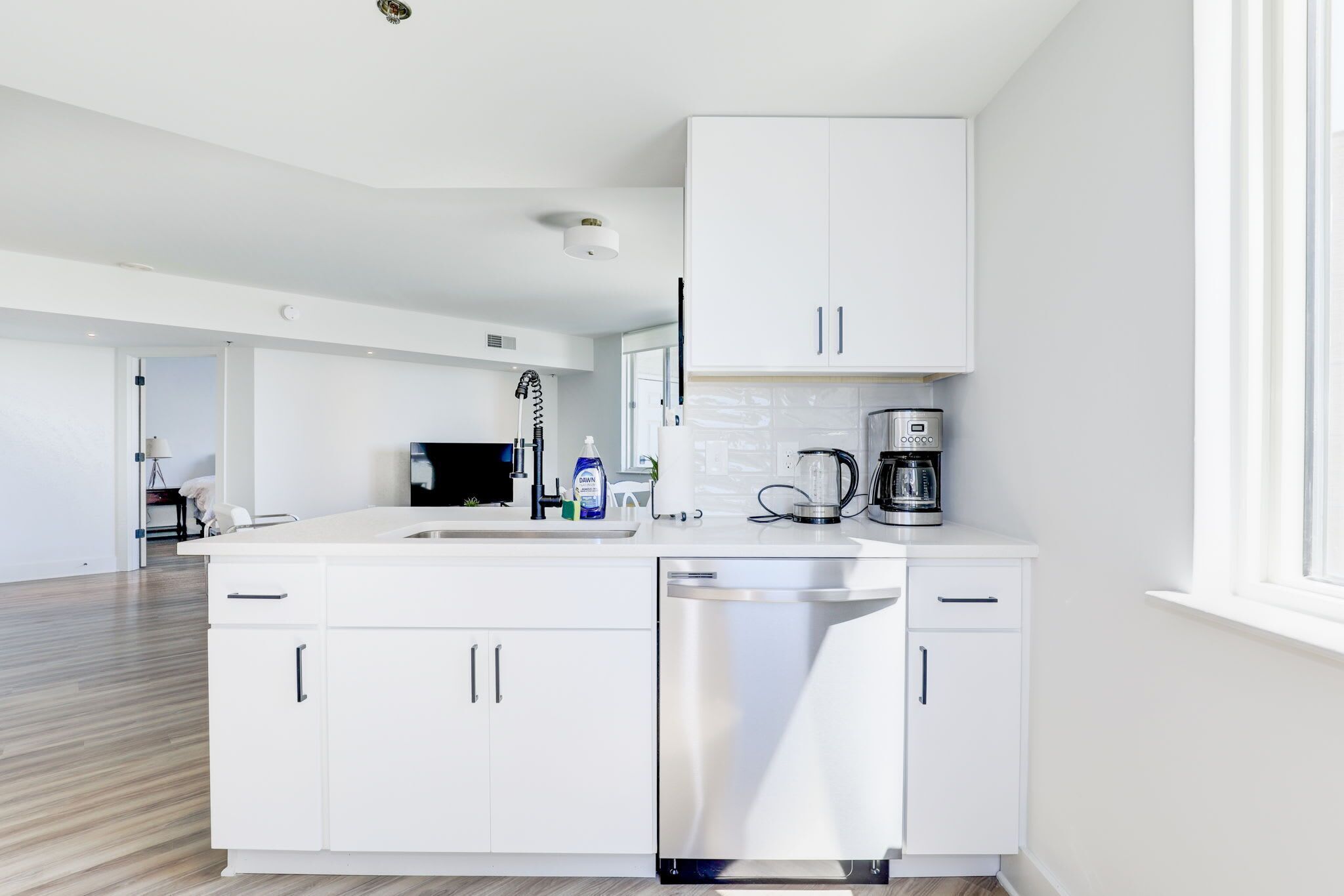 Una cocina moderna con armarios blancos, lavavajillas y cafetera.