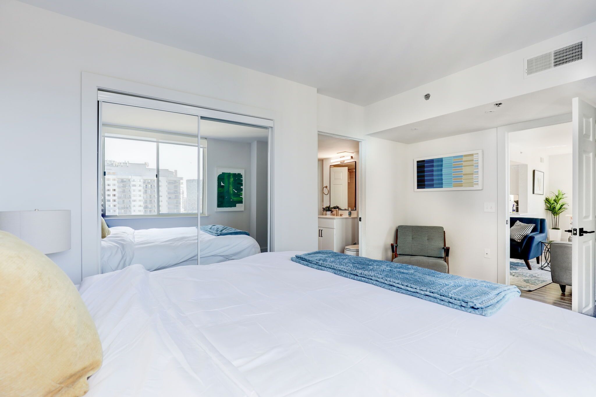 A hotel room with a large bed, a wardrobe, a chair, and a view of the city.