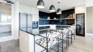 Een moderne keuken met een centraal eiland, barkrukken, hanglampen en uitzicht op de aangrenzende woonkamer.