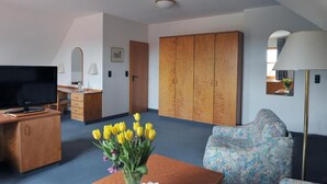 A hotel room with a television, wooden desk, wardrobe, sofa, and a vase of yellow flowers. - Hotel Grüner Baum (Pommersfelden)