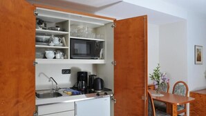 A compact kitchen with a microwave, stove, and sink, and a dining area with a table and chairs. - Hotel Grüner Baum (Pommersfelden)