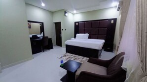 A compact hotel room with a bed, a desk, a chair, and a small table. - Kelvic Systems Apartments (Abuja)