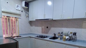 A kitchen with grey cabinets, a gas stove, a sink, and a window with yellow frames. - Kelvic Systems Apartments (Abuja)